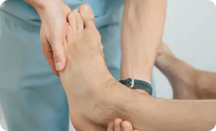 A clinician in scrubs supporting and examining a patient's bare foot