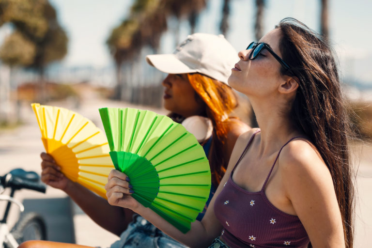 Two women using folding hand fans to cool off outdoors in the summer heat