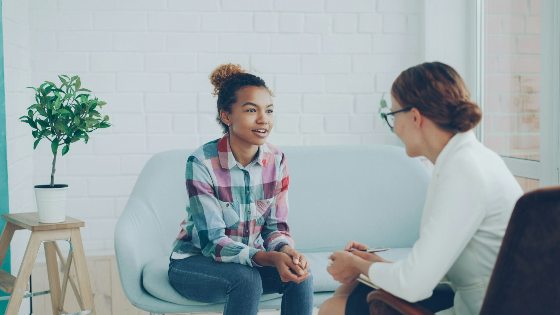 A smiling young woman talks with a counselor who listens and takes notes in a bright, relaxed office