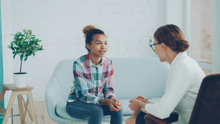 A smiling young woman talks with a counselor who listens and takes notes in a bright, relaxed office