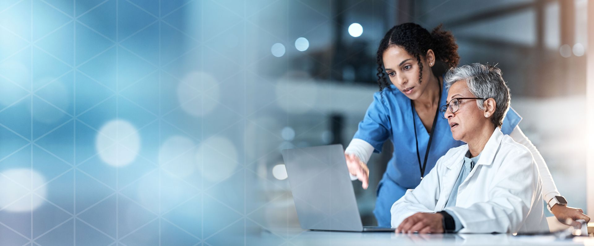 Two clinicians look at a laptop screen together while reviewing patient information