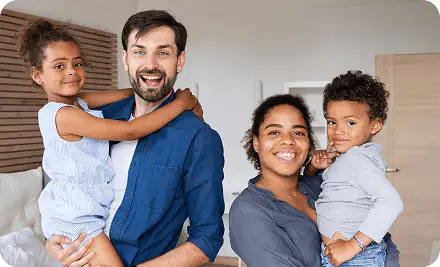 A mother and father each holding a smiling young child in a bright bedroom