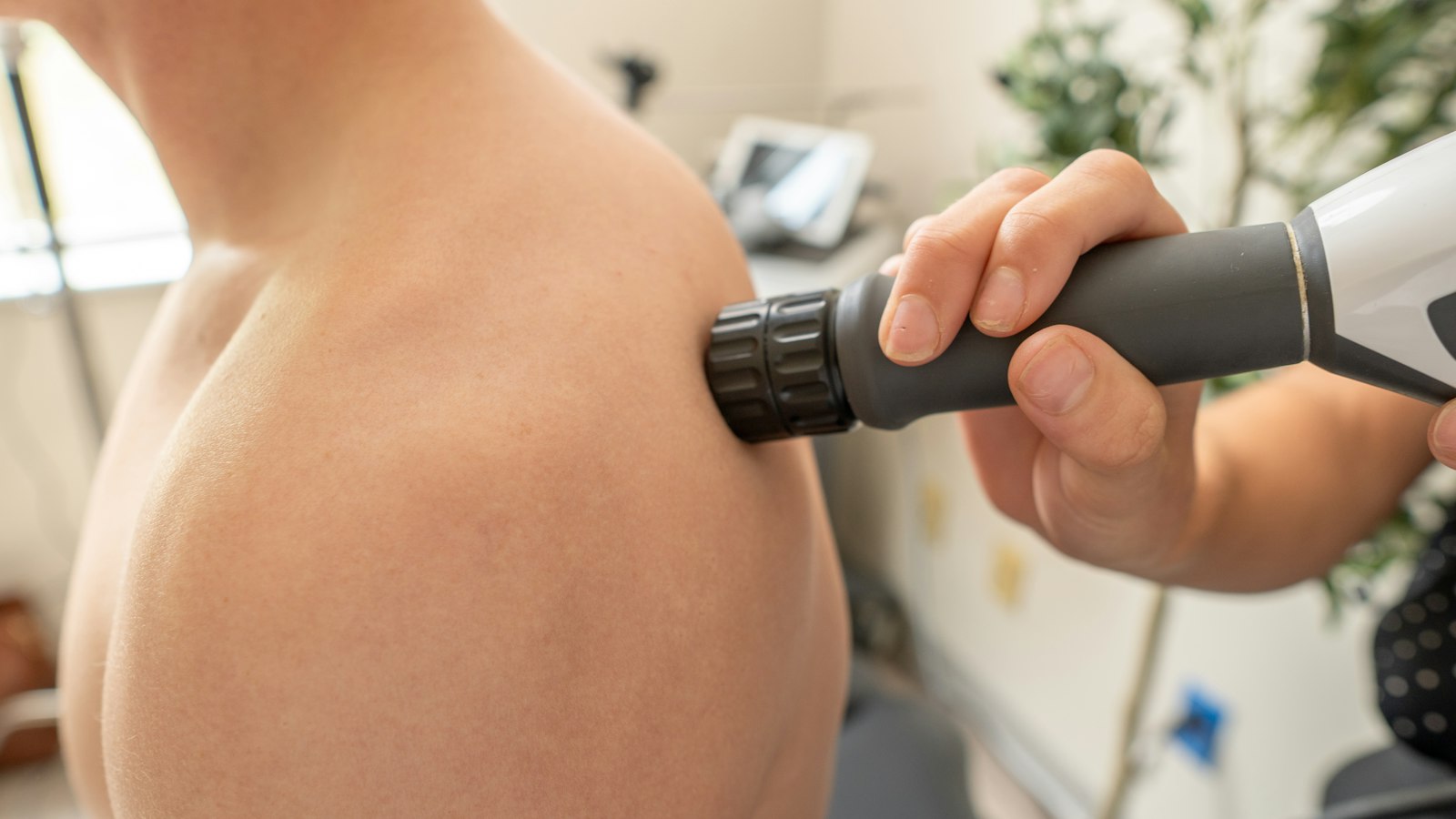 Clinician treating a patient’s shoulder with a handheld therapy device