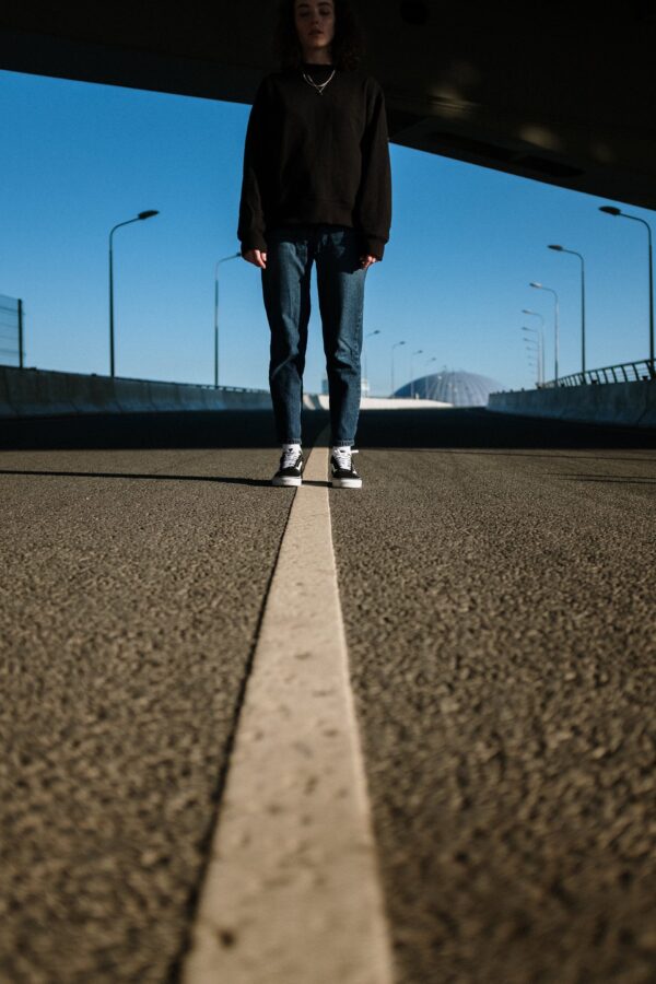 A person stands at the center line of a roadway beneath an overpass