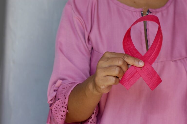 Woman holding a pink awareness ribbon, representing cancer screening services